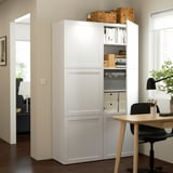 Unité de rangement BESTÅ blanche avec étagères et portes réglables, contenant des livres et des boîtes. Il est fixé au mur, mettant en valeur son organisation.