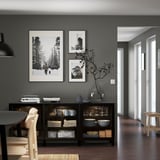 Salle à manger moderne avec buffet BESTÅ noir, exposant des plats, des tasses et des décorations. Accompagné de photos de nature encadrées et de chaises en bois.