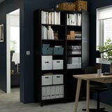 Unité de rangement BESTÅ noire avec étagères et armoires, contenant des livres, des boîtes et des objets décoratifs. Personnalisable et fixé au mur pour plus de sécurité.