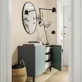 Couloir contemporain avec unité de rangement BESTÅ en bleu et noir ; portes ouvertes, panier en osier, miroir et plante.