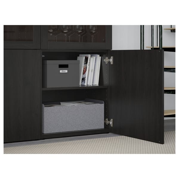 Une armoire BESTÅ noire avec une porte ouverte, mettant en valeur des étagères réglables contenant des boîtes de rangement grises et des livres.