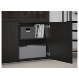 Une armoire BESTÅ noire avec une porte ouverte, mettant en valeur des étagères réglables contenant des boîtes de rangement grises et des livres.