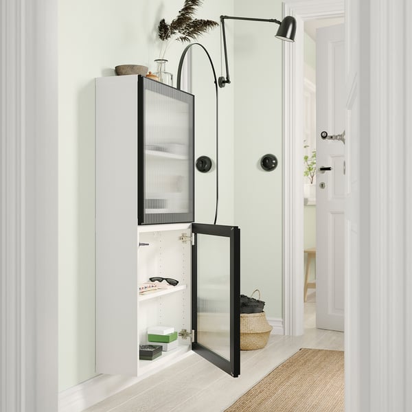 Unité de rangement BESTÅ moderne blanche avec porte en verre et charnières réglables, stylisée avec divers articles.