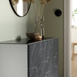 Plateau en verre BESTÅ avec bol et vase de fleurs séchées contre mur végétal.