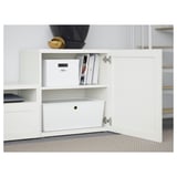 Armoire BESTÅ blanche avec porte ouverte, présentant des étagères réglables, des boîtes de rangement et un système de gestion des câbles.