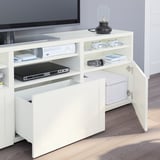 Meuble TV BESTÅ avec étagères ouvertes et rangements, y compris l’électronique et les contrôleurs.