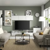Salon moderne avec télévision à écran plat sur l’unité BESTÅ, deux canapés lumineux, une table basse en verre et des murs verts.