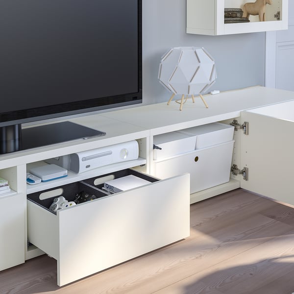 Meuble TV blanc avec tiroir ouvert révélant des manettes de jeu et des jeux ; Peut contenir un téléviseur, une console et dispose d’étagères réglables et d’un système de gestion des câbles.
