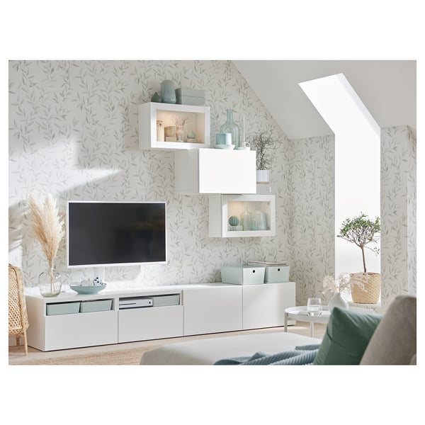 Salon moderne avec meuble TV BESTÅ, étagères réglables, tiroirs et armoires murales. Accents bleu clair et papier peint à motifs de feuilles.