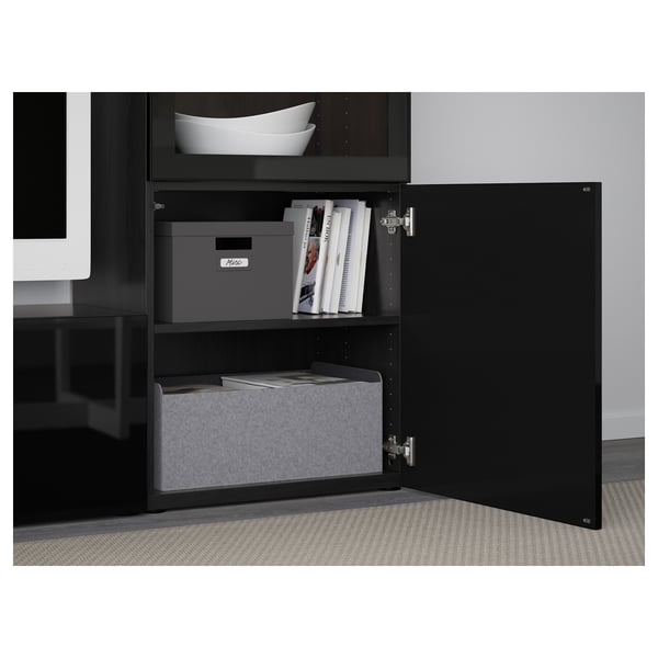 Armoire BESTÅ noire avec porte ouverte révélant des boîtes de rangement, des magazines et des étagères pour un espace de travail organisé.