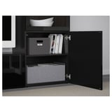 Armoire BESTÅ noire avec porte ouverte révélant des boîtes de rangement, des magazines et des étagères pour un espace de travail organisé.