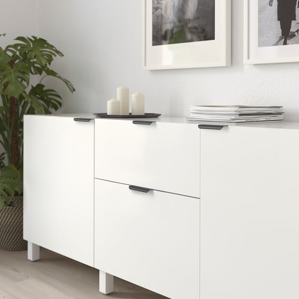 Armoire blanche avec des poignées noires, des bougies décoratives, des livres empilés et de la plante à côté.
