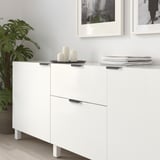 Armoire blanche avec des poignées noires, des bougies décoratives, des livres empilés et de la plante à côté.