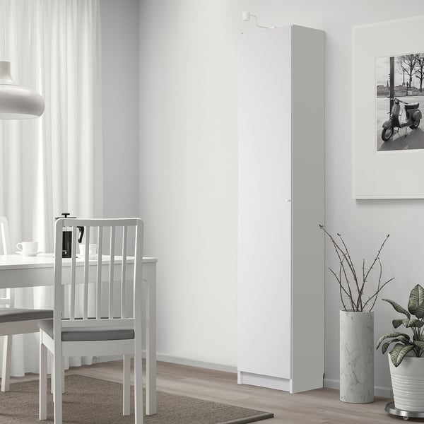 Bibliothèque BILLY blanche dans une pièce minimaliste, à côté d’une table à manger avec des chaises, un design élégant et haut, à côté d’une grande fenêtre avec des rideaux.