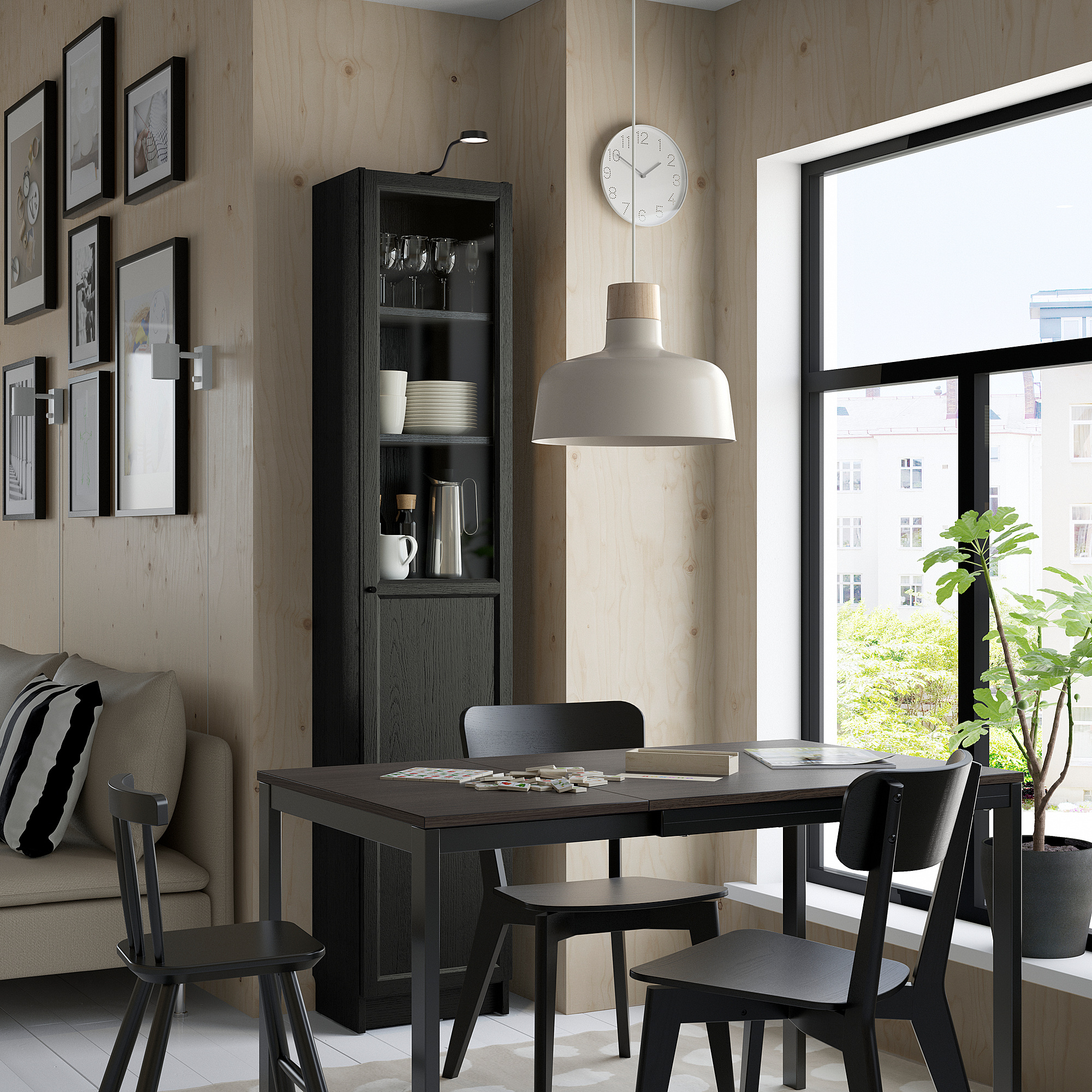 Salle à manger moderne avec table noire, chaises, armoire BLY, lampe, horloge, canapé, plante.