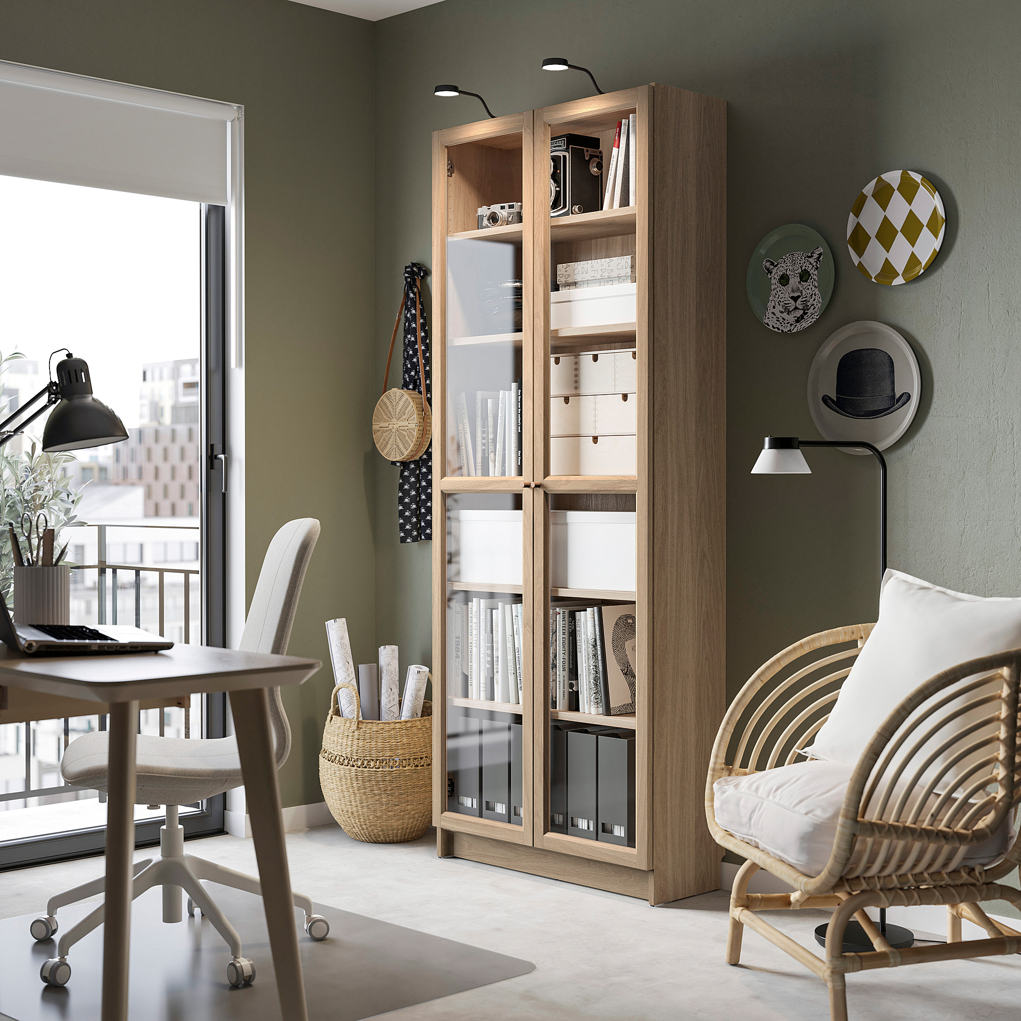 Bibliothèque BILLY en bois clair avec portes vitrées, près d’une chaise blanche et d’une petite table, décorée d’assiettes et de vases.