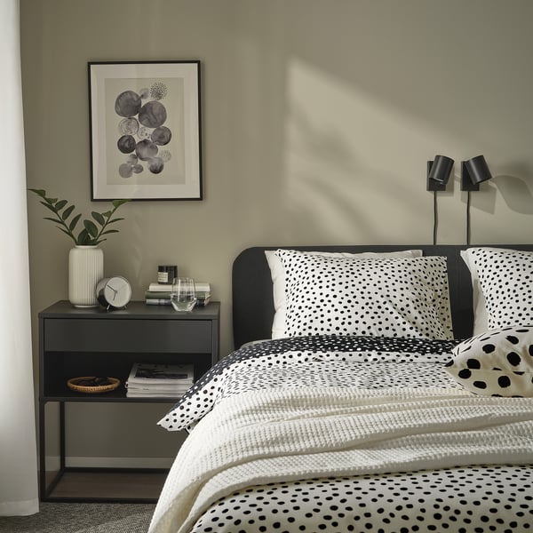 Chambre élégante avec couette BJÖRKGRÅMAL, plante, livres et lampes.