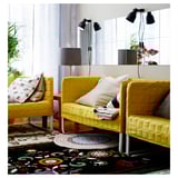 Salon lumineux avec des chaises jaunes sur un tapis coloré, entouré de miroirs et de plantes.