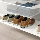 Une étagère en maille blanche permet de ranger soigneusement des jeans pliés, des baskets vertes et des chaussures de ville marron sur une étagère blanche sous un tiroir en maille mural.