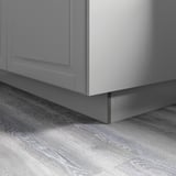 Armoire de cuisine grise avec finition laquée lisse, fixée au sol en bois avec grain visible, démontrant un style minimaliste et une surface facile à nettoyer.