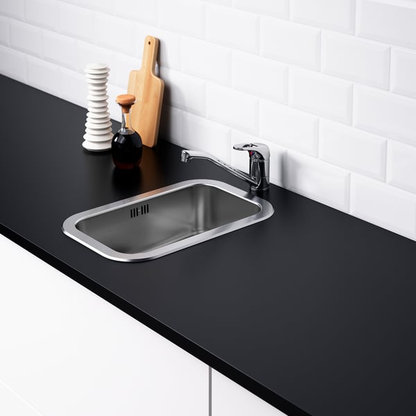 Évier en acier inoxydable avec robinet, comptoir noir, coussin sonore, mur en tuiles blanches.