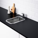 Évier en acier inoxydable avec robinet, comptoir noir, coussin sonore, mur en tuiles blanches.
