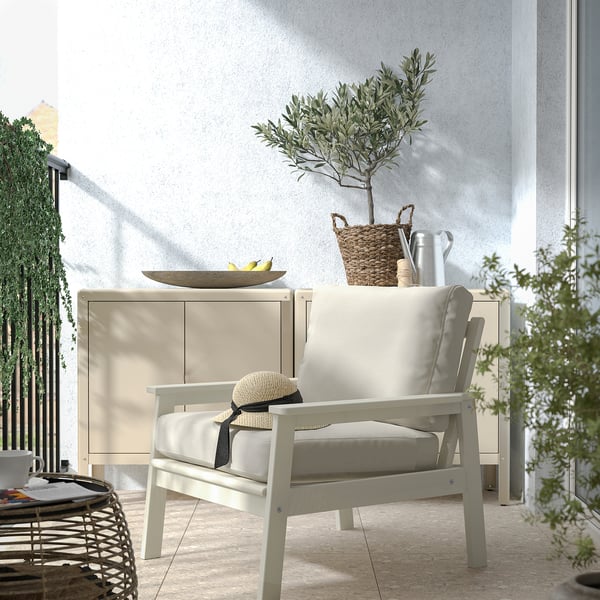Fauteuil d’extérieur BONDHOLMEN beige clair avec coussins ; buffet blanc ; panier et plante sur le dessus. Balcon confortable.