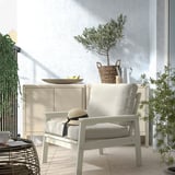 Fauteuil d’extérieur BONDHOLMEN beige clair avec coussins ; buffet blanc ; panier et plante sur le dessus. Balcon confortable.