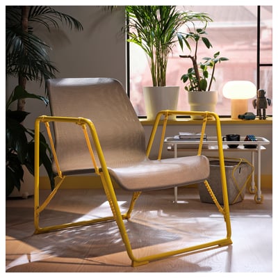 Chaise BRÄNNBOLL : jaune vif, pieds en acier inclinés, dossier en maille, grande, à côté d’une petite table avec lampe et plantes.