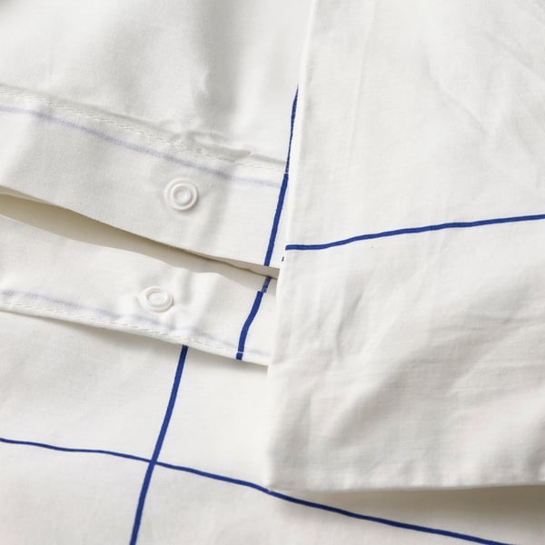 Gros plan d’un drap de lit blanc avec de fines lignes bleues, avec des attaches en forme de boutons.