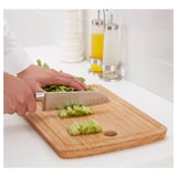 Une personne coupe des légumes verts sur une planche à découper en bambou à l’aide d’un couteau en acier inoxydable. Le couteau est doté d’une lame en acier damas.