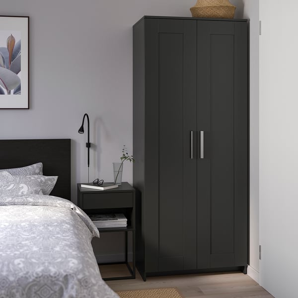 Armoire BRIMNES noire moderne entre lit ikea et table d’appoint, rangement élégant et pratique.