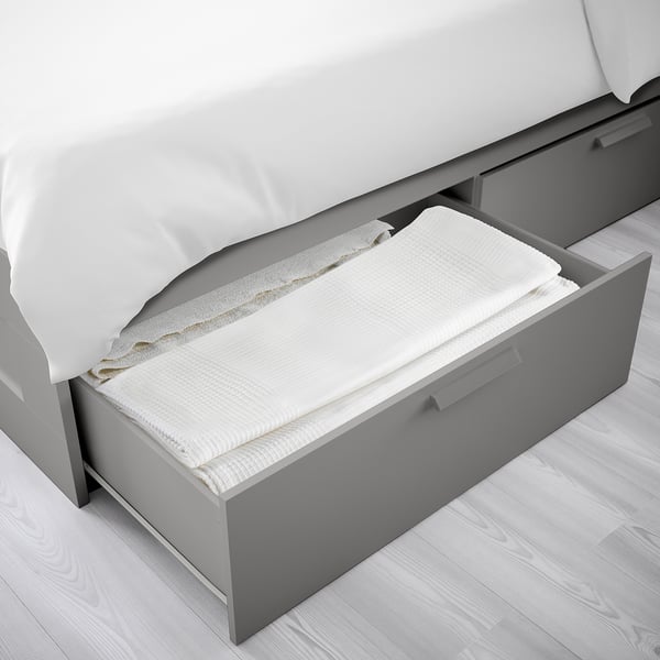 Cadre de lit avec tiroir ouvert, montrant les draps pliés, offrant un rangement sous le lit.