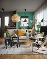 Espace de vie confortable avec canapé beige, oreillers colorés, parquet et mur végétal. Tapis lumineux, suspension en osier et plantes suspendues.