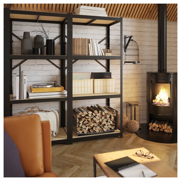 Salon confortable avec étagères BROR noires remplies de livres et de décorations, cheminée, chaise orange, plancher de bois.