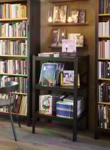 Étagère en métal noir contenant de nombreux livres et objets de décoration. Design moderne et robuste, idéal pour la maison ou le bureau.