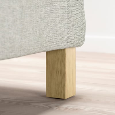 Cadre de lit recouvert de tissu gris clair avec des pieds en bois clair.