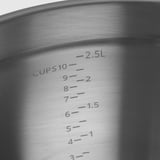 Gros plan du bol doseur en acier inoxydable, gravé avec les mesures de tasse et de litre, mettant en valeur la qualité et la précision.