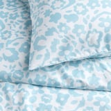 Draps de lit fleuris bleu clair sur fond blanc. Tissu doux, infroissable, soigneusement plié.