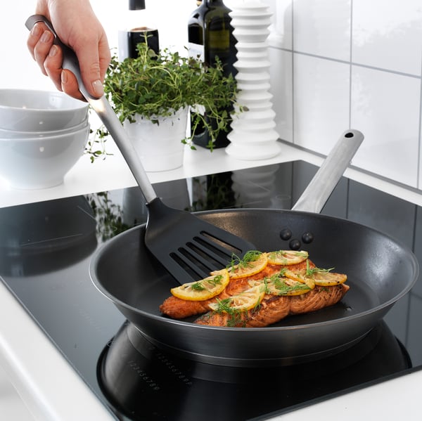 Tenant la main spatule retournant du poisson au citron dans une poêle noire sur la cuisinière.