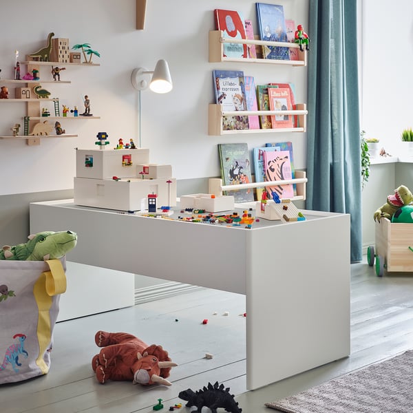 Salle de jeux pour enfants avec table DUNDRA blanche, étagères en bois, jouets colorés et animaux en peluche ; Scène lumineuse et ludique.