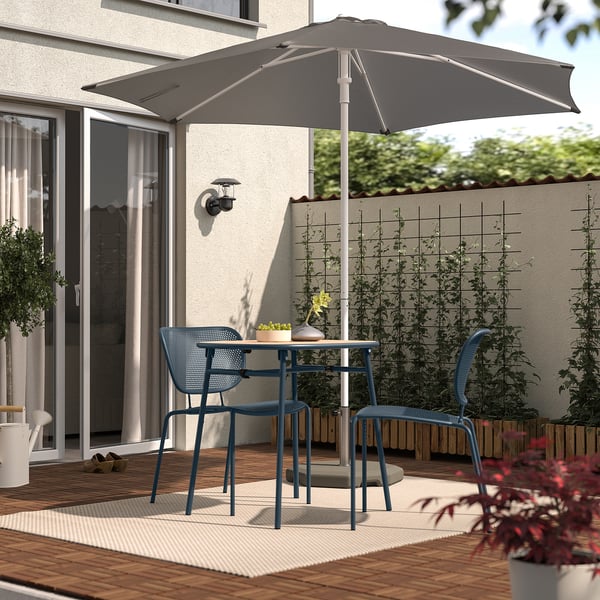 Configuration de patio confortable avec parasol gris, chaises bleues, table en bois et plantes.