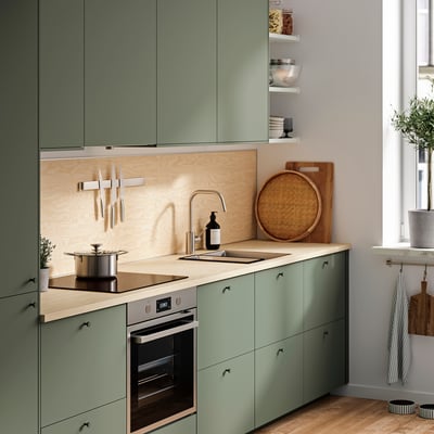 Cuisine moderne avec placards verts EKBACKEN, comptoir en bois, four en acier inoxydable et couteaux suspendus.