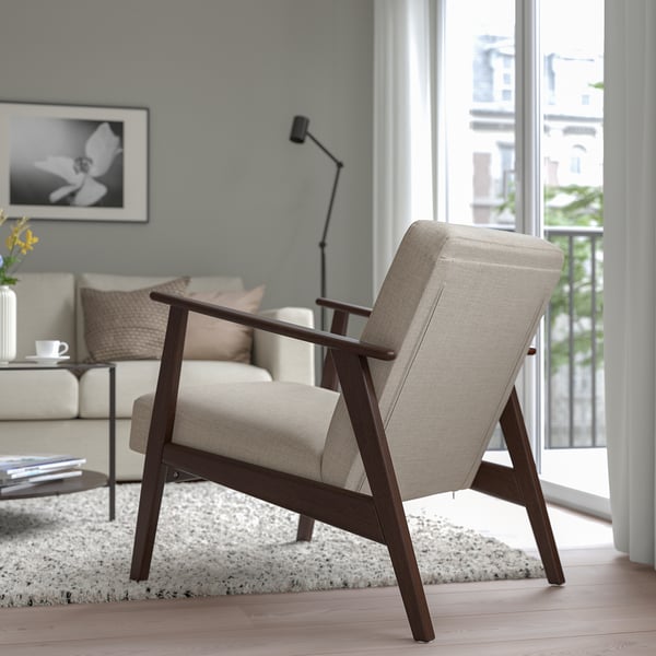 Salon moderne avec fauteuil beige EKENÄSET, cadre en bois, coussins moelleux, grande fenêtre adjacente et canapé confortable avec oreillers et une table.