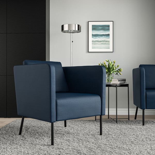 Salon moderne avec fauteuils bleus, table d’appoint, lampadaire et peinture marine.