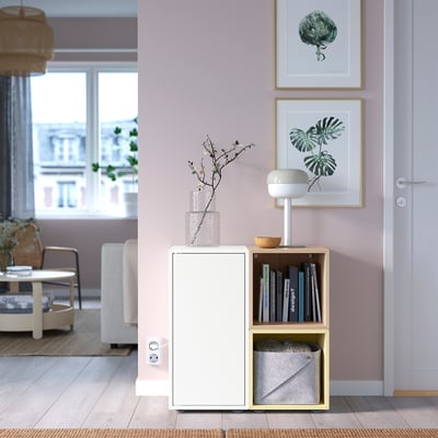 Petite unité de rangement EKET blanche avec des sections ouvertes et fermées sous l’art mural. Tient des livres et des objets décoratifs près d’une porte.