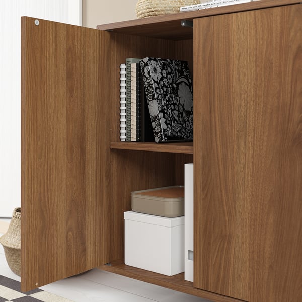 Une armoire en bois EKET avec une porte ouverte, révélant des étagères avec des boîtes de rangement et des livres.