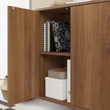 Une armoire en bois EKET avec une porte ouverte, révélant des étagères avec des boîtes de rangement et des livres.