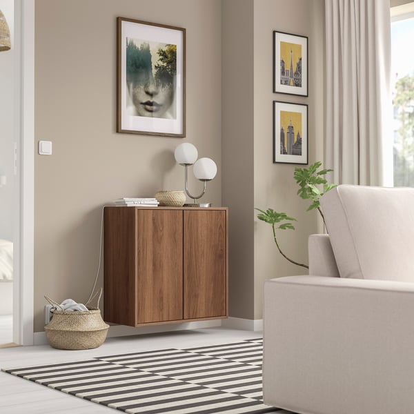 Chambre moderne avec armoire en bois EKET, tapis noir-blanc et fauteuil gris. Des œuvres d’art et des plantes décorent l’espace.