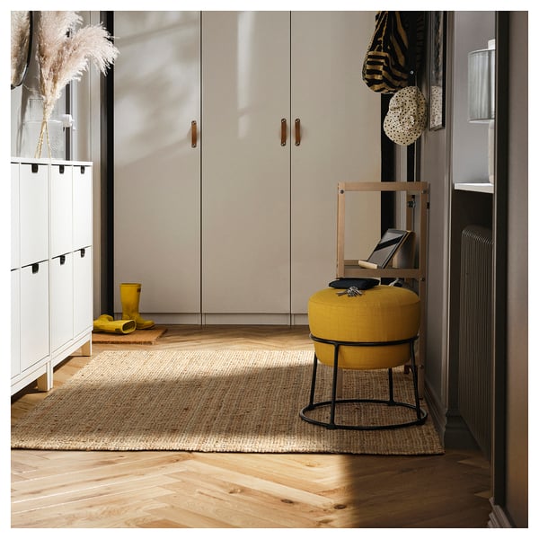 Pouf EMMISLÖV jaune vif dans une entrée moderne, doté d’un cadre en métal élégant et d’un siège en tissu moelleux, entouré d’unités de rangement et de décoration.